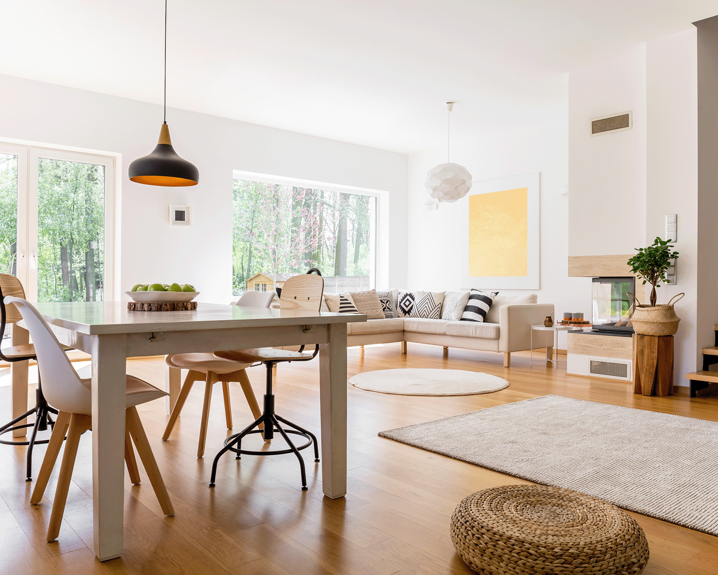Black designed lamp above dining table in spacious living room with braided pouf on wooden floor